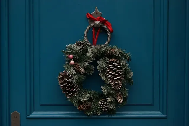 Front door Christmas wreath designed with pinecone and red ribbon 