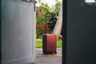 red and black luggage bag outside the front door of house, get ready to leave home for vacation