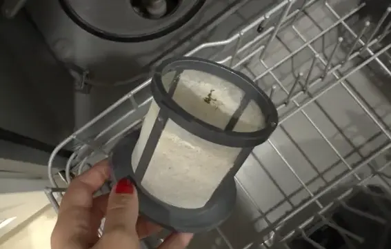 Close-up of a used dishwasher filter removed from the machine, showing buildup and debris.