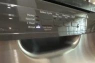 Close-up of a stainless steel dishwasher control panel showing the rinse cycle light turned on.