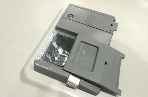 Open dishwasher detergent compartment showing leftover soap residue inside.