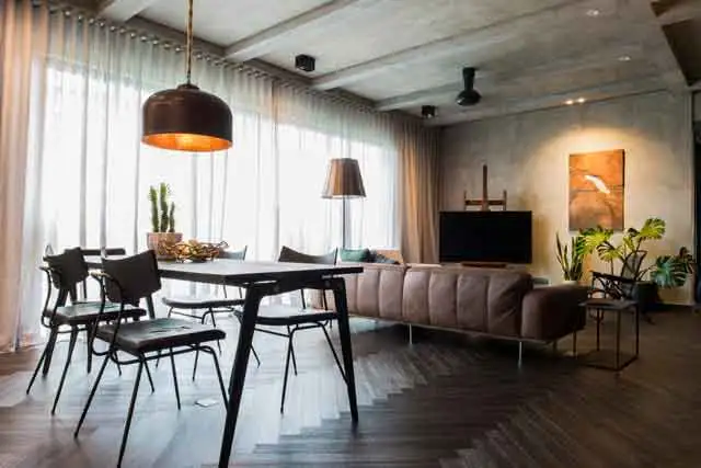 Open-concept living and dining area featuring a sleek black dining set under a warm pendant light, a contemporary brown sofa facing a TV, and a statement art piece on the wall, demonstrating how a focal point anchors home design.