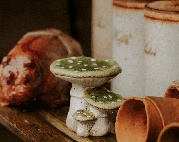 Rustic ceramic mushroom ornaments with green caps and white spots displayed alongside terracotta pots and vintage kitchen canisters.