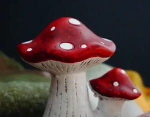 Decorative ceramic mushrooms with vibrant red caps and white spots, featuring textured white stems, used as whimsical home accents.